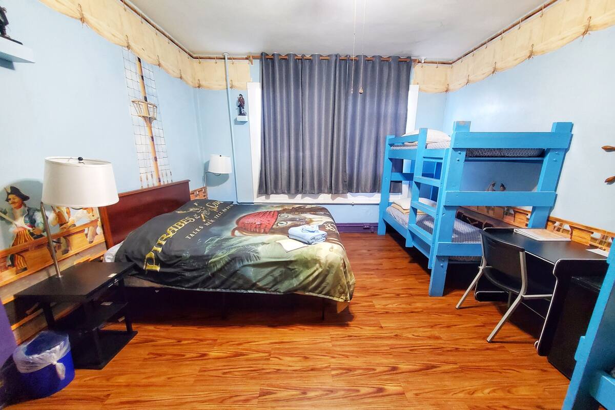 Quarto com cama, beliches, escrivaninha, cadeira, luminária e prateleira na parede.