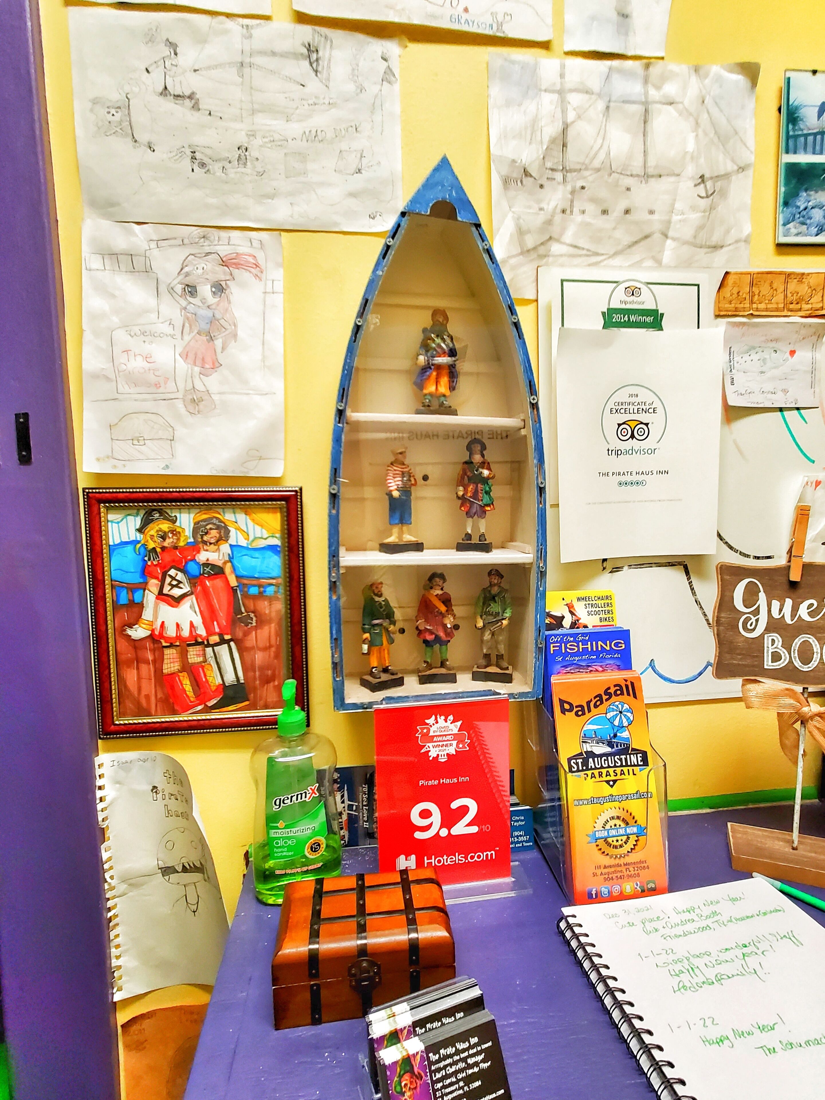 Una habitación con una cama, una mesita con una botella, un cuadro enmarcado y un cartel.