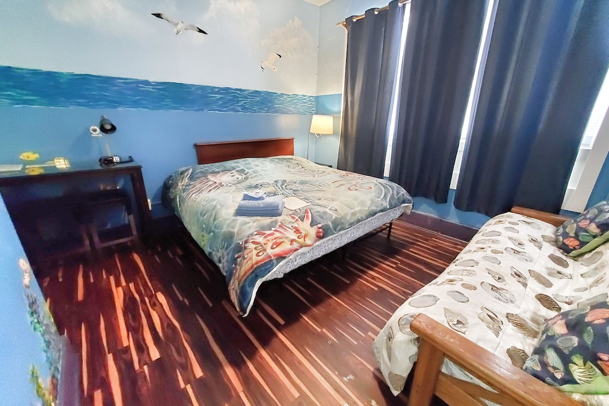 Quarto com uma cama, mesa de cabeceira de madeira, abajur e janela com cortinas.