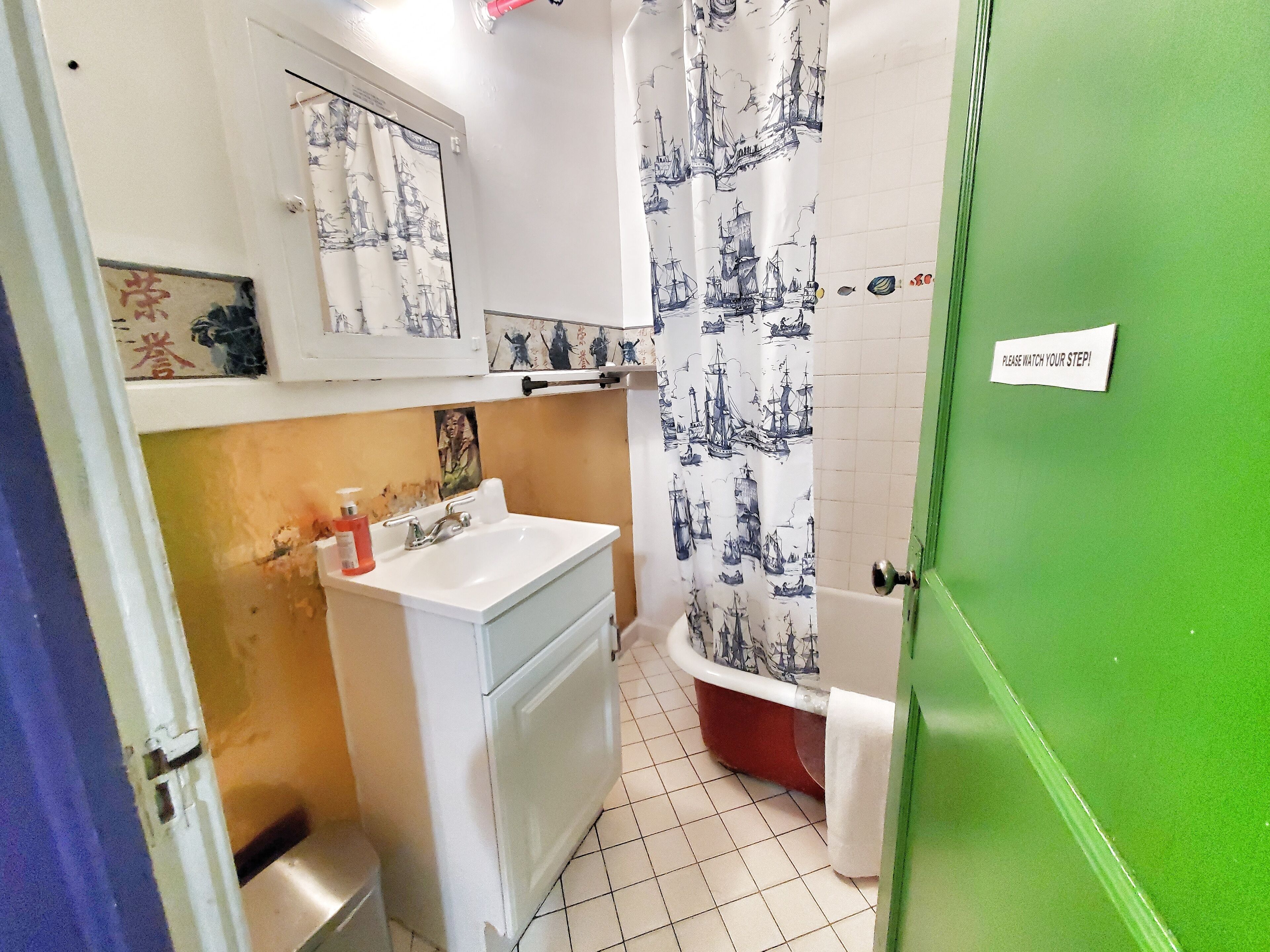 A bathroom with a white sink, a red bathtub, and a green door.