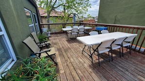 Een houten terras met buitenmeubilair, inclusief tafels en stoelen, omringd door plantenpotten.