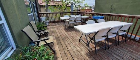 Una terraza de madera con mobiliario exterior, incluyendo mesas y sillas, rodeada de plantas en macetas.