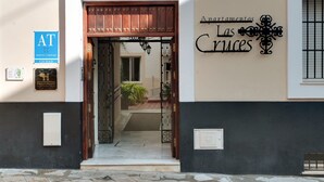 Entrada de hotel con puerta de madera, un cartel que dice "At" y otro cartel para "Apartamentos Las Cruces".