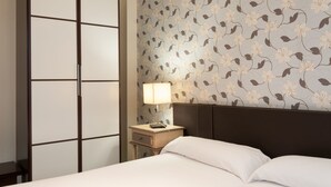 Una habitación de hotel con una cama, una mesita de noche con lámpara y un armario.