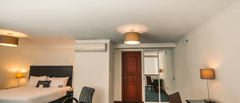 A hotel room with a bed, a chair, a desk, and a lamp.