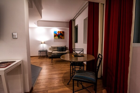 A modern living room with a round table and chairs, a sofa, a lamp, and a colorful abstract painting on the wall. - El Polo Hotel & Suites (Santiago de Surco)