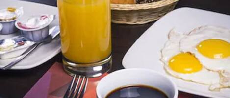 Un desayuno con un vaso de jugo de naranja, una taza de café y un plato de huevos sobre una mesa con un mantel individual.