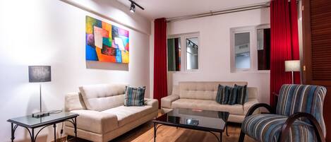 Una sala de estar con dos sofás, una mesa de centro, una lámpara y un cuadro abstracto de colores en la pared.