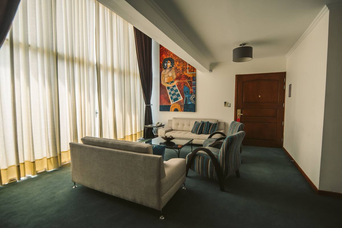Un salon avec un canapé, un fauteuil et une table basse. Il y a un tableau au mur et une porte à l’arrière-plan.