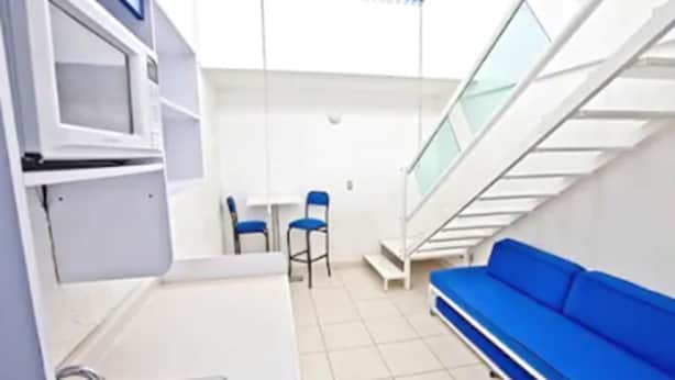 A compact kitchen with a sink, two chairs, a small table, and a blue sofa. - Hotel H Américas Guadalajara (Guadalajara)