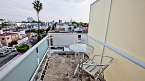 A balcony with a metal table and chairs, a view of a cityscape, and a palm tree. - Hotel H Américas Guadalajara (Guadalajara)