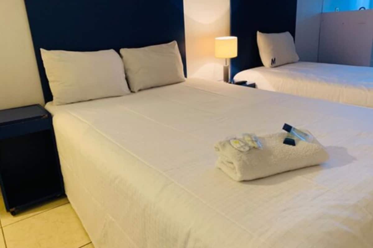 A hotel room with two beds, a nightstand, and a lamp.
