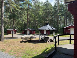 A campground with red cabins, a picnic table, and a covered seating area.