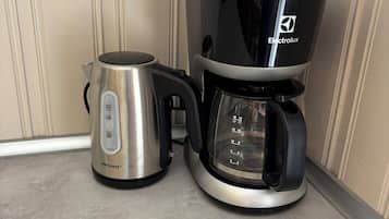A coffee maker with a black drip tray and a stainless steel pot on a countertop.