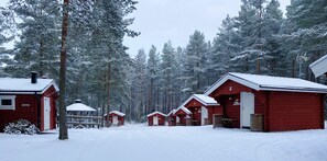 A row of red cabins with white trim, numbered from 2 to 7, in a snowy forest setting. - Hyltena Stugby (Jönköping)