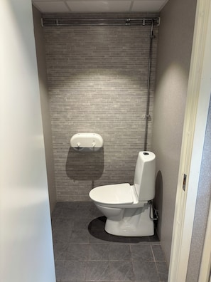 A small, modern bathroom with a toilet and a hand dryer mounted on the wall.