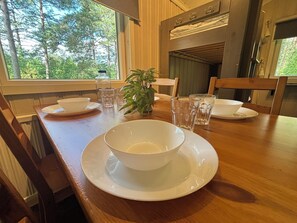 A dining table set with white plates, bowls, and glasses, with a potted plant in the center.
