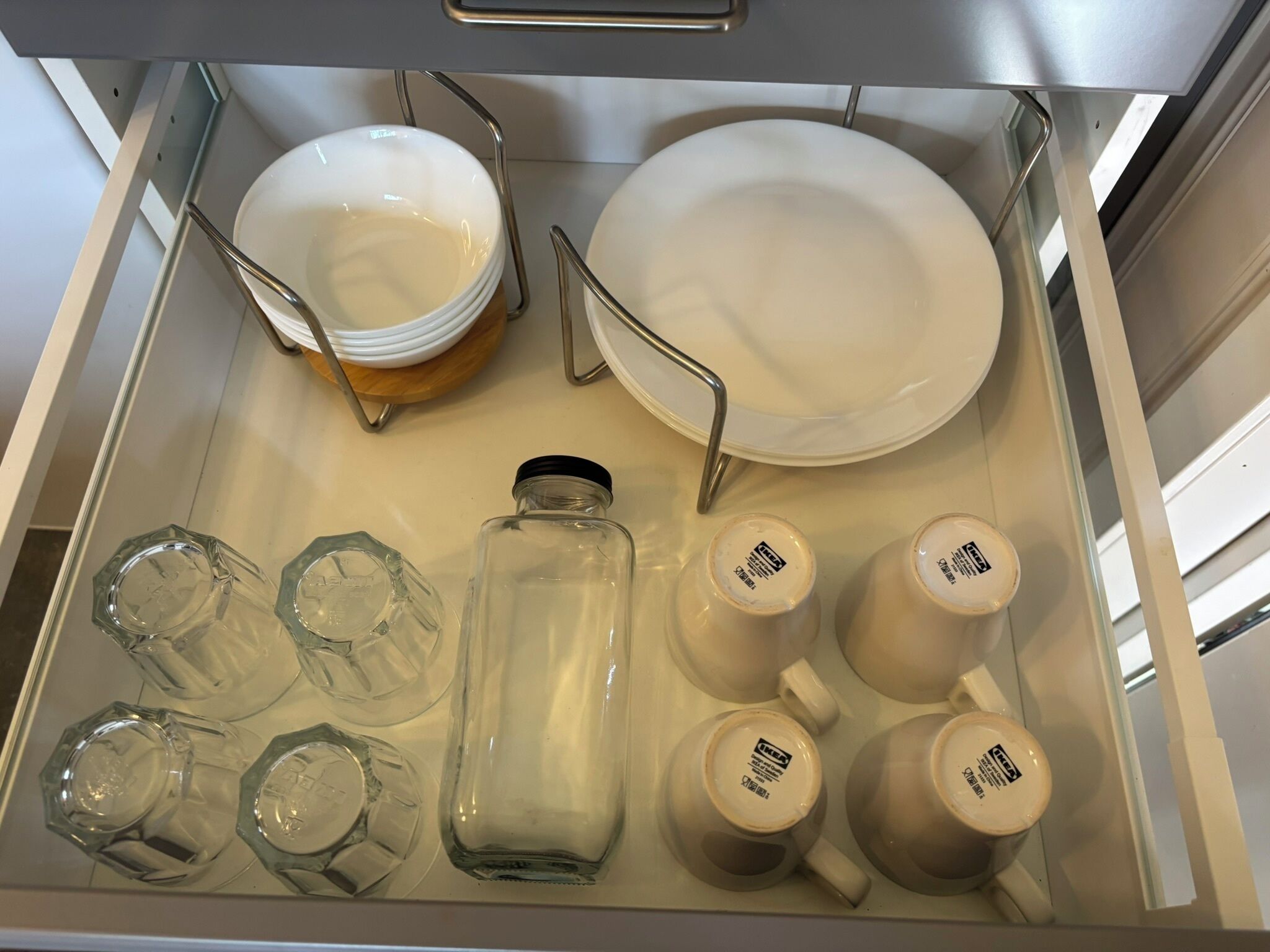 Un cajón de cocina con platos, tazones y cristalería blanca.