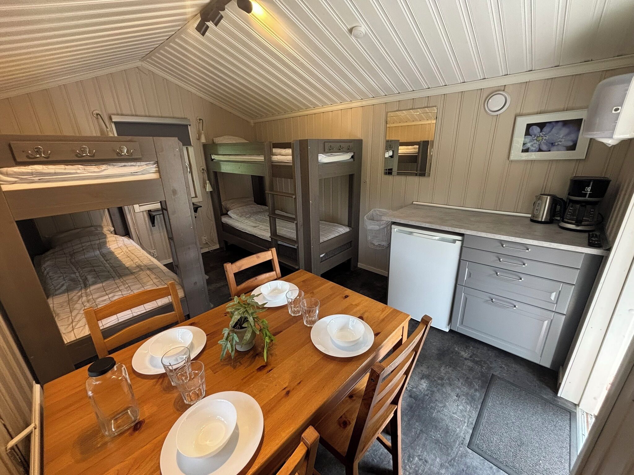 Een compacte kamer met stapelbedden, een klein kitchenette en een eettafel voor twee personen.