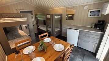 Een compacte kamer met stapelbedden, een klein kitchenette en een eettafel voor twee personen.