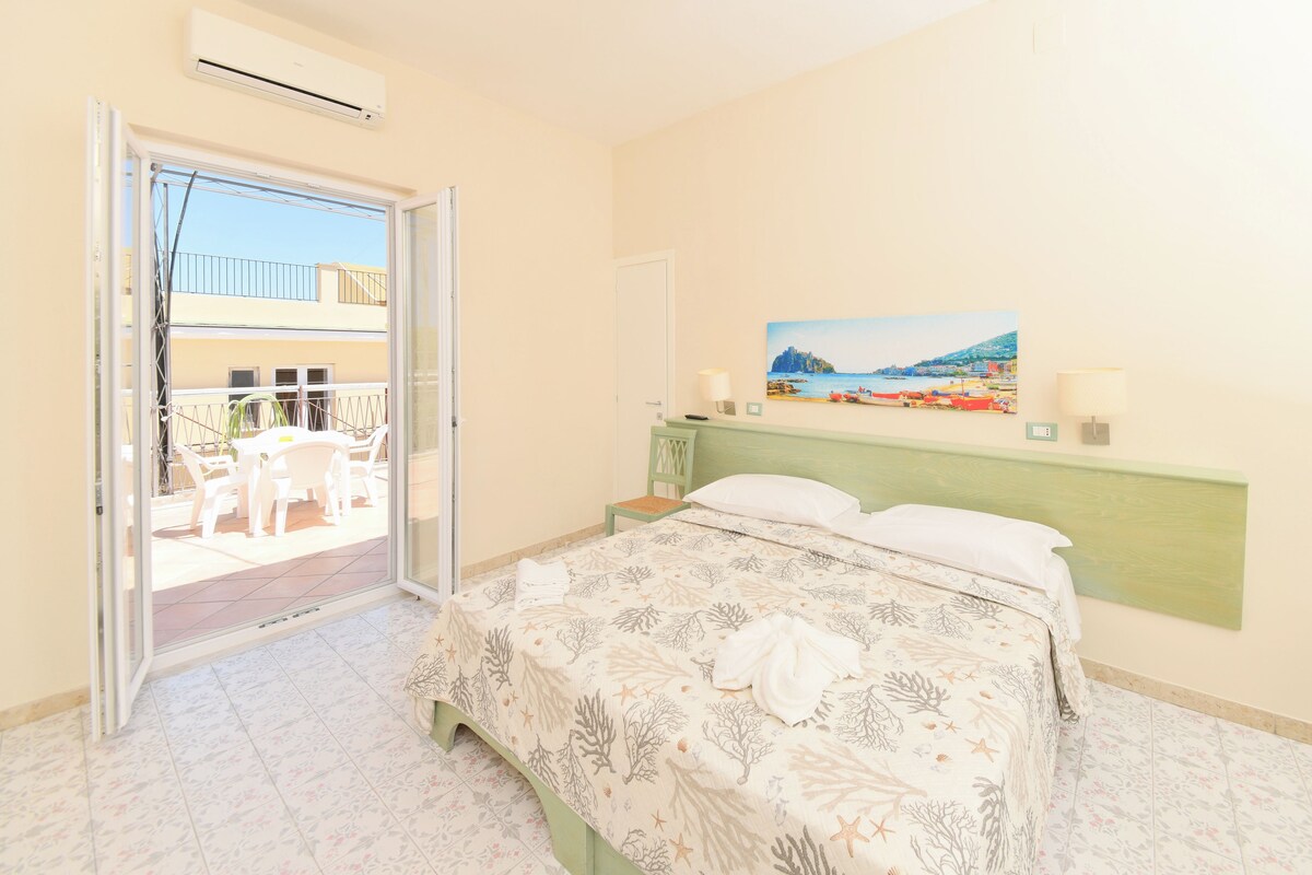 A bedroom with a bed, a painting, and a view of a balcony with outdoor furniture.