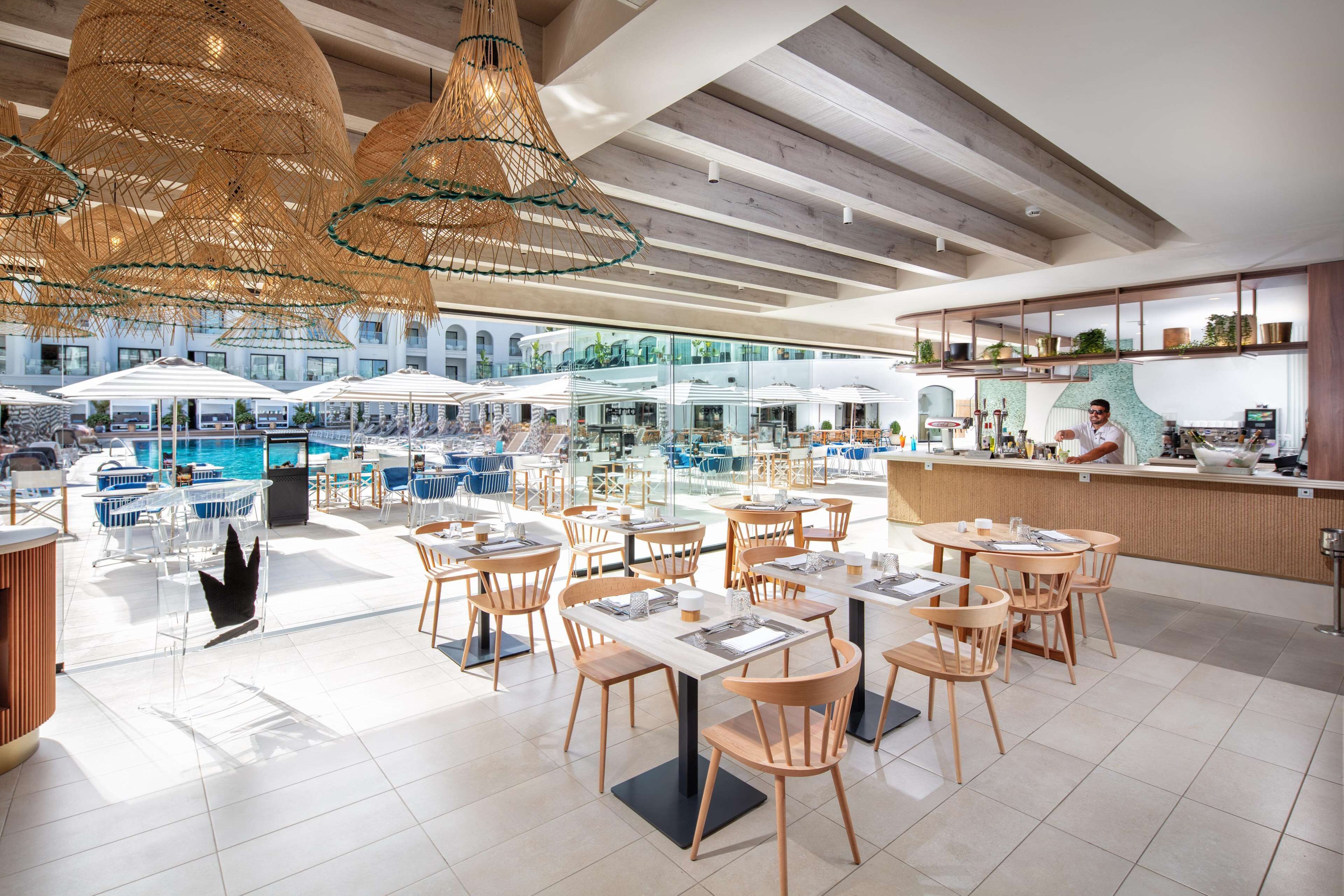 Ein moderner Essbereich im Freien mit Tischen und Stühlen, im Hintergrund ein Pool und eine Bar.