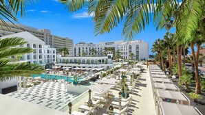 Un complexe hôtelier doté d’une piscine, de chaises longues et de palmiers.