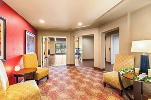 A hotel lobby with patterned carpet, yellow patterned chairs, a table with a vase, and a lamp. - Quality Inn Blackwell Ok (Blackwell)