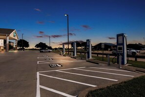 A parking lot with electric vehicle charging stations, marked parking spaces, and a gas station in the background.