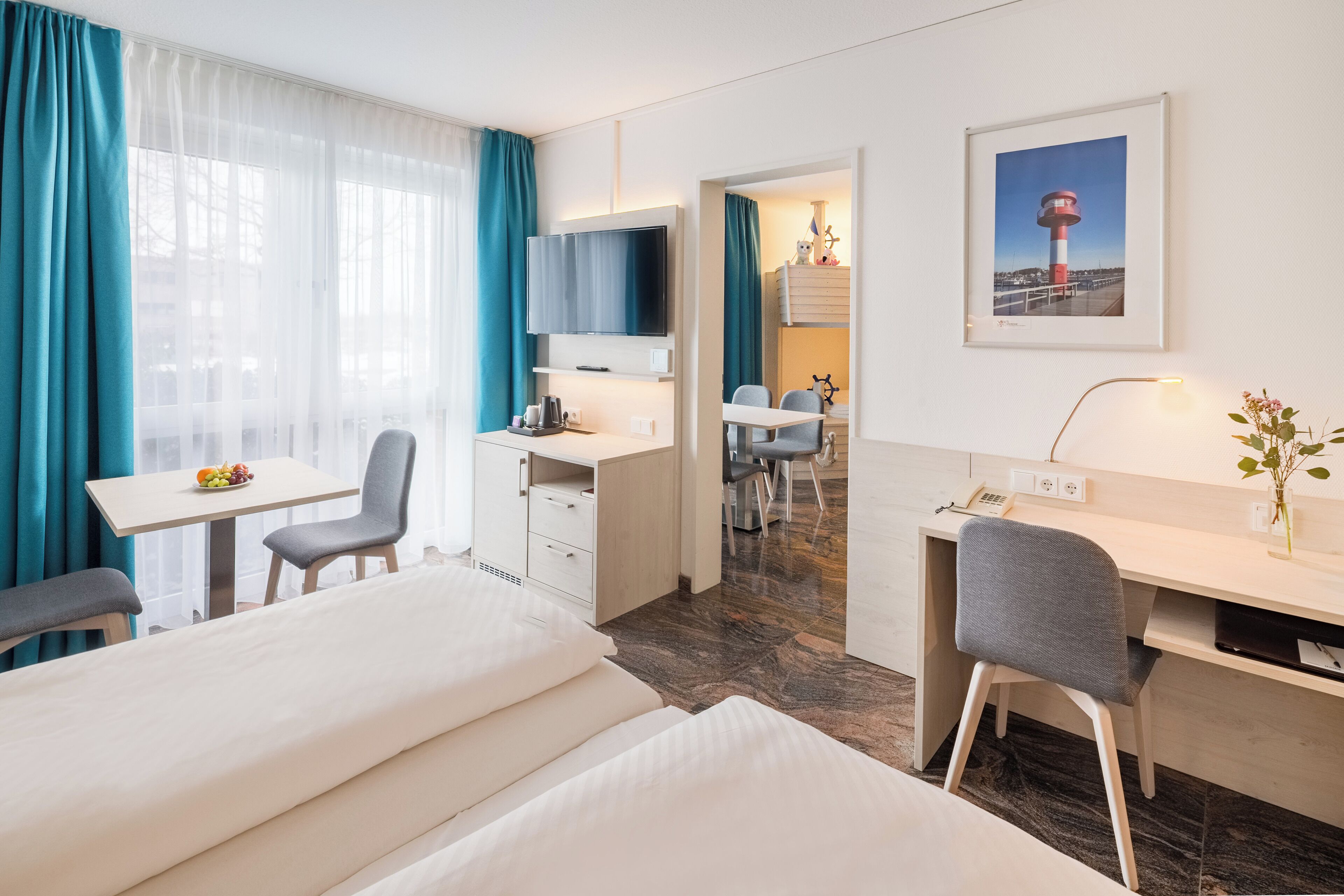 Habitación de hotel con cama, escritorio, silla, televisor y zona de comedor con sillas y mesa.