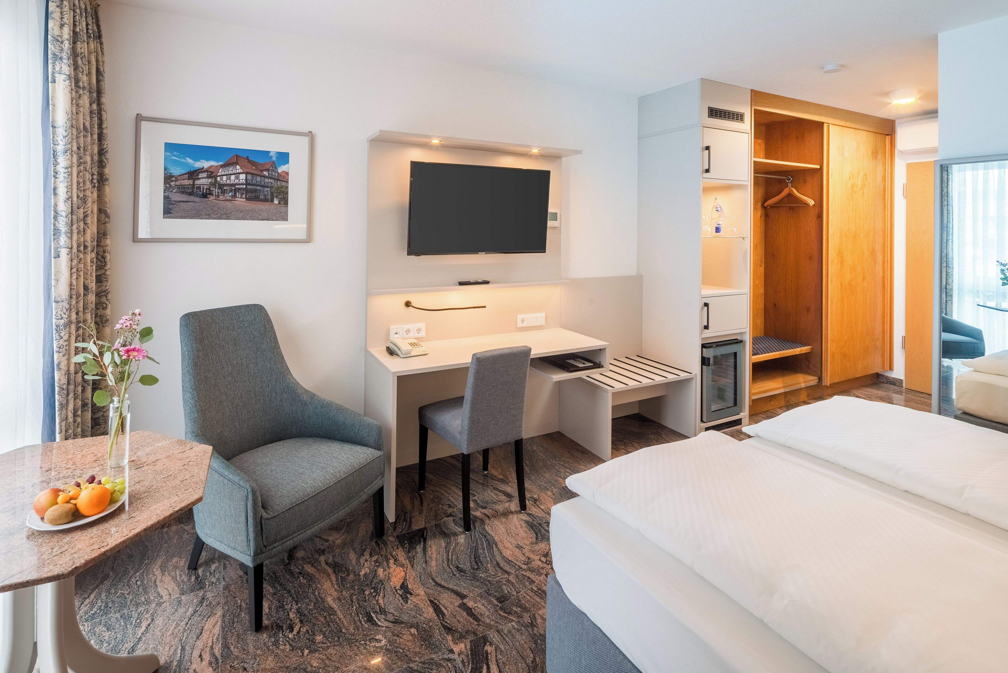 Hotelkamer met een bed, een bureau met een stoel, een tv boven het bureau, een kledingkast en een klein tafeltje met fruit.