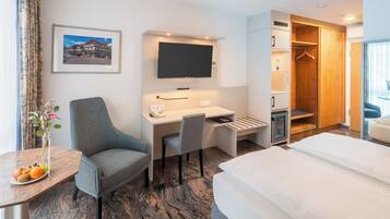 Hotelkamer met een bed, een bureau met een stoel, een tv boven het bureau, een kledingkast en een klein tafeltje met fruit.