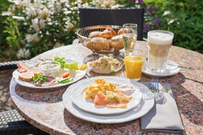 Desayuno servido en una mesa al aire libre, con platos de comida, un vaso de jugo y un vaso de leche.