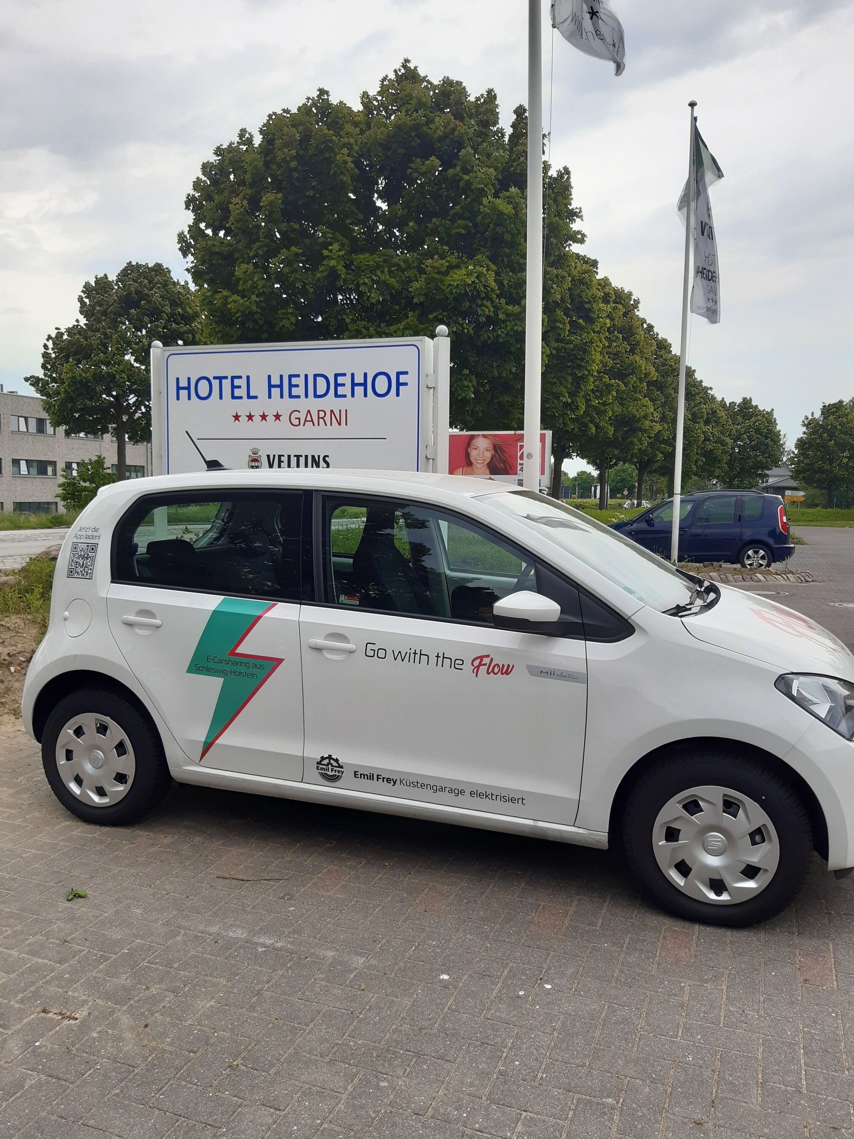 En vit bil med en skylt på bakluckan där det står ”HOTEL HEIDEHOF” och ”GARNI”.