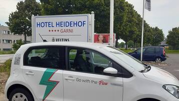 En vit bil med en skylt på bakluckan där det står ”HOTEL HEIDEHOF” och ”GARNI”.