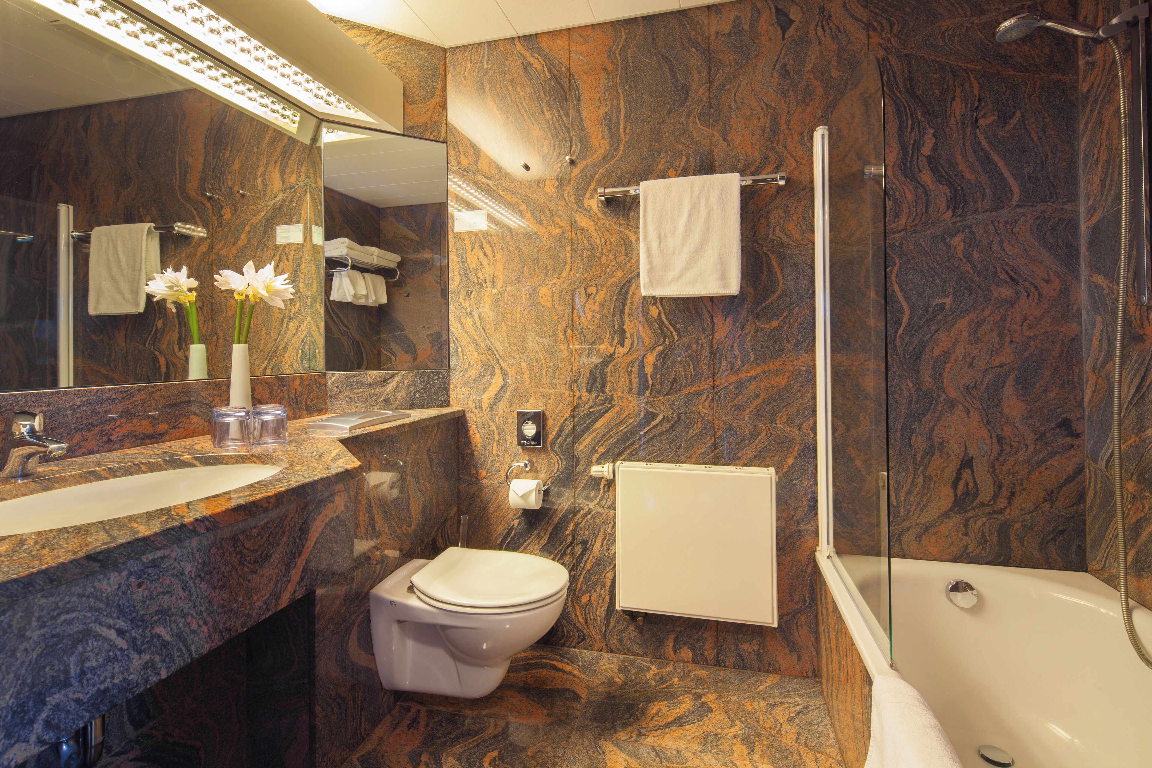 Ein Badezimmer mit Marmorwand, Waschbecken, Toilette, Dusche und Spiegel.