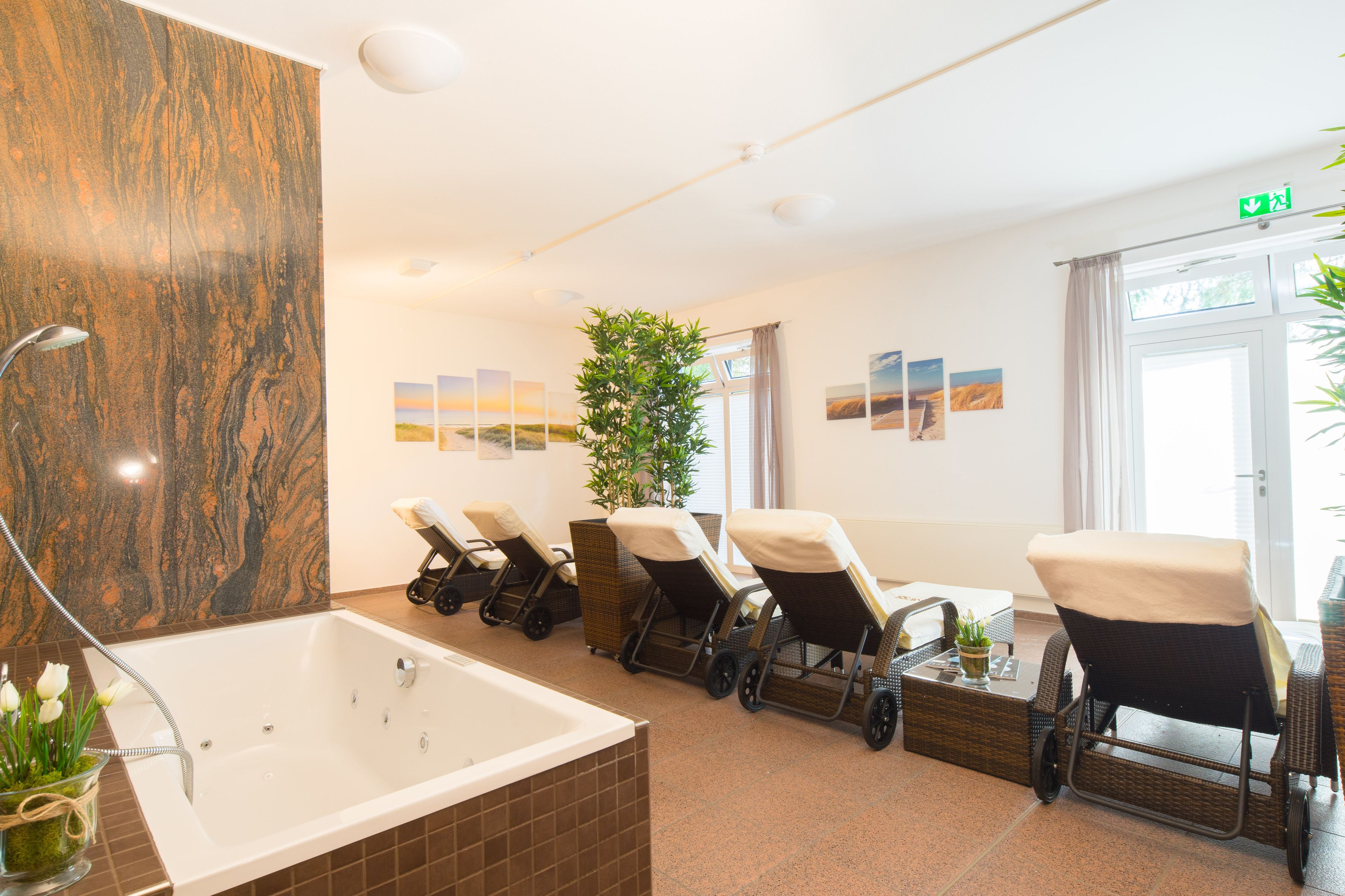 Ein Spa-Raum mit einer großen Badewanne, mehreren Massagesesseln, einer Topfpflanze und Kunstwerken an den Wänden.