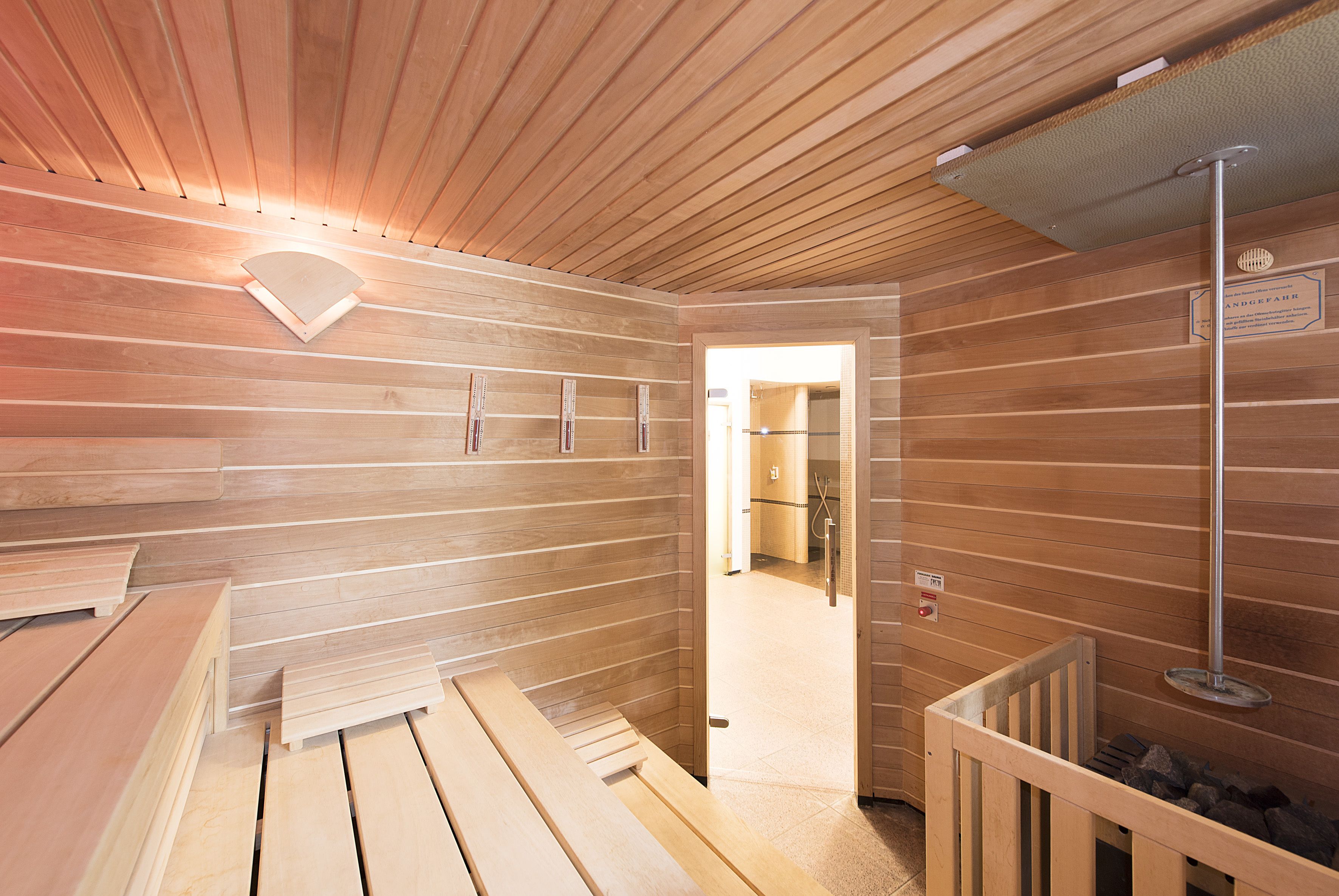 A sauna room with wooden benches, a bench heater, and a shower area.