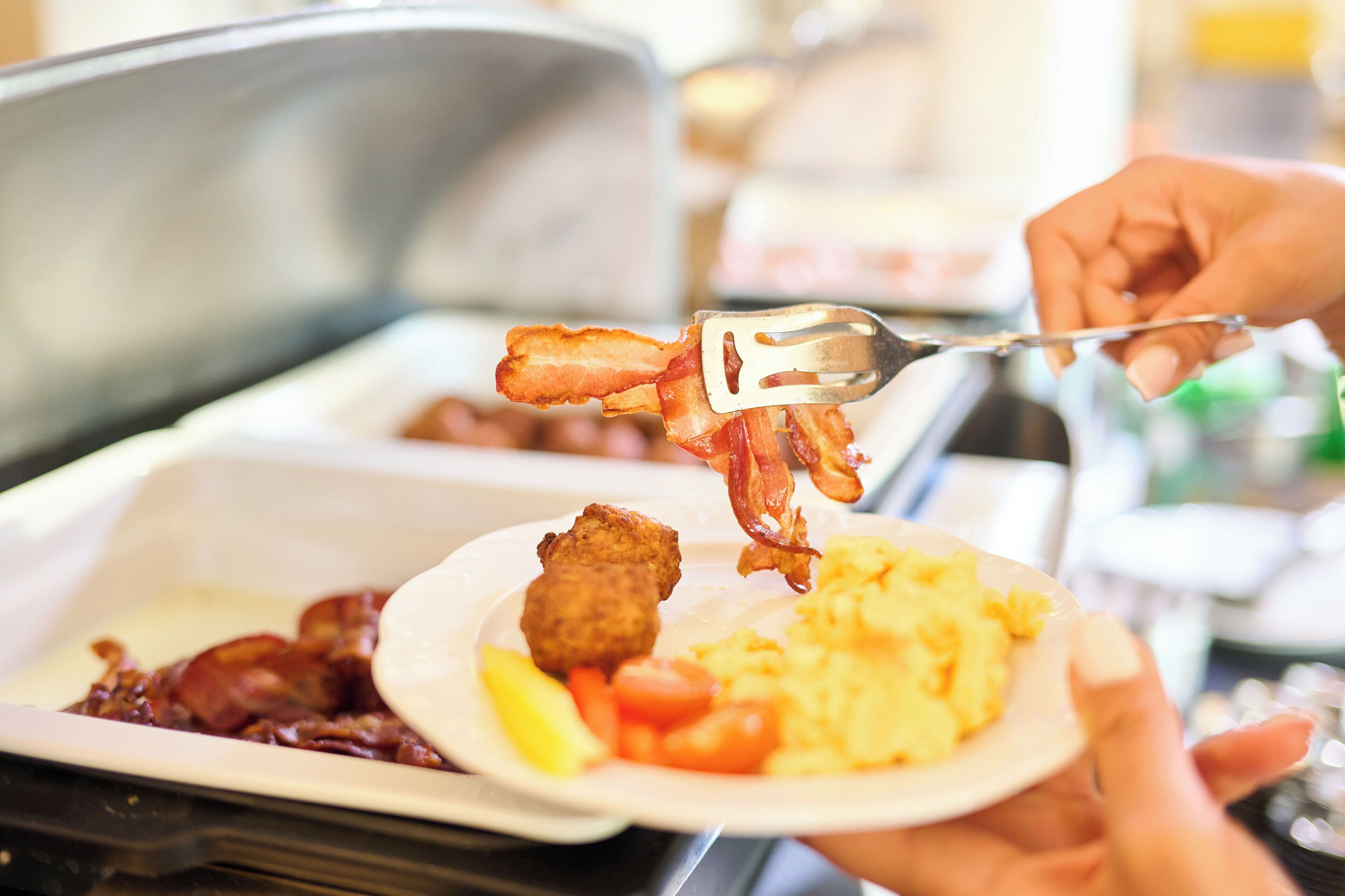 A breakfast plate with scrambled eggs, bacon, and a fried item, possibly a chicken piece, on a tray.