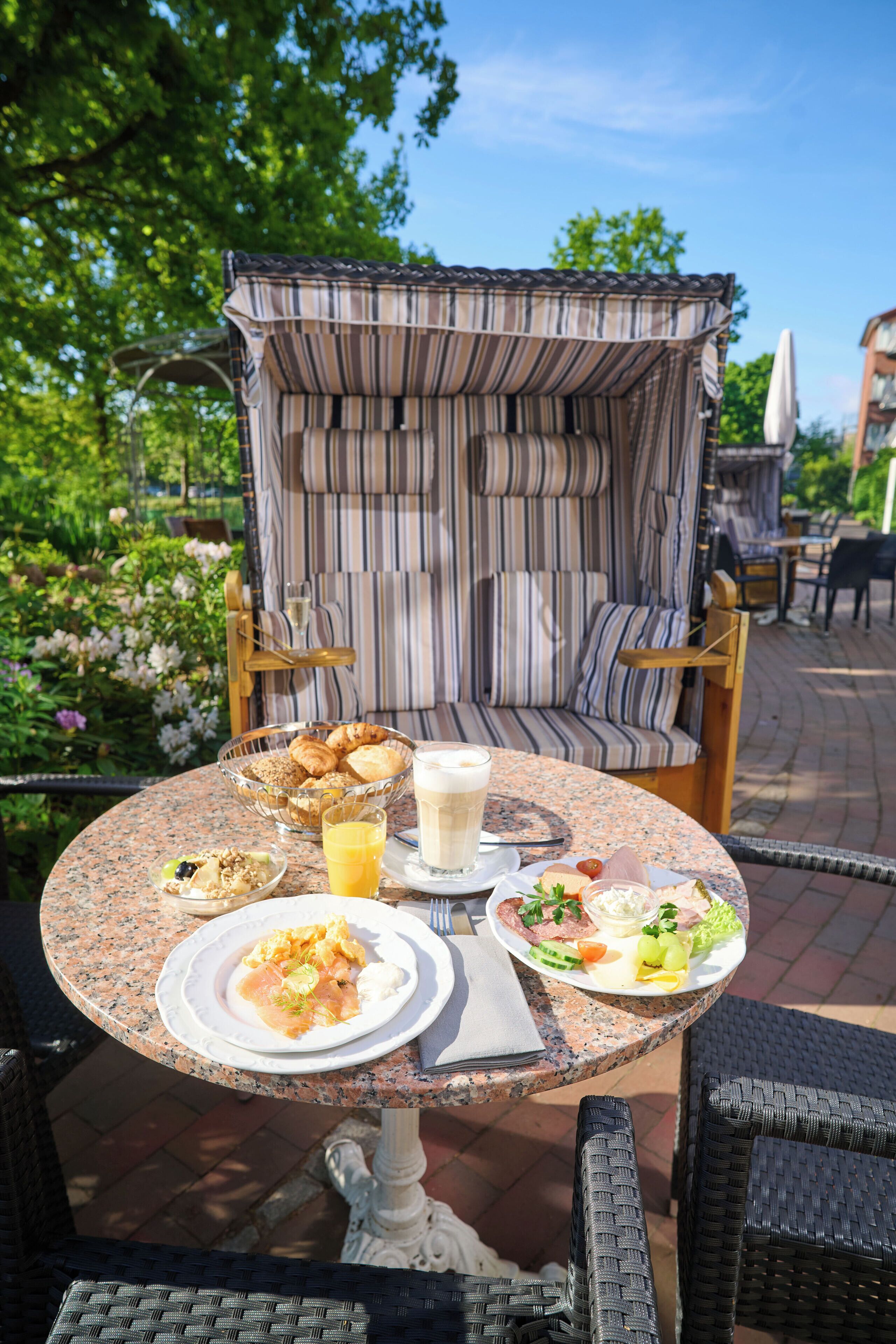 An outdoor dining area with a table set for breakfast, including plates of food, a glass of orange juice, and a bowl of pastries.