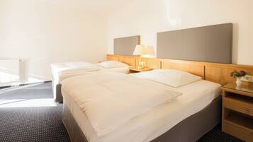 A hotel room with two beds, a wooden headboard, bedside tables with lamps, and a small vase with flowers.
