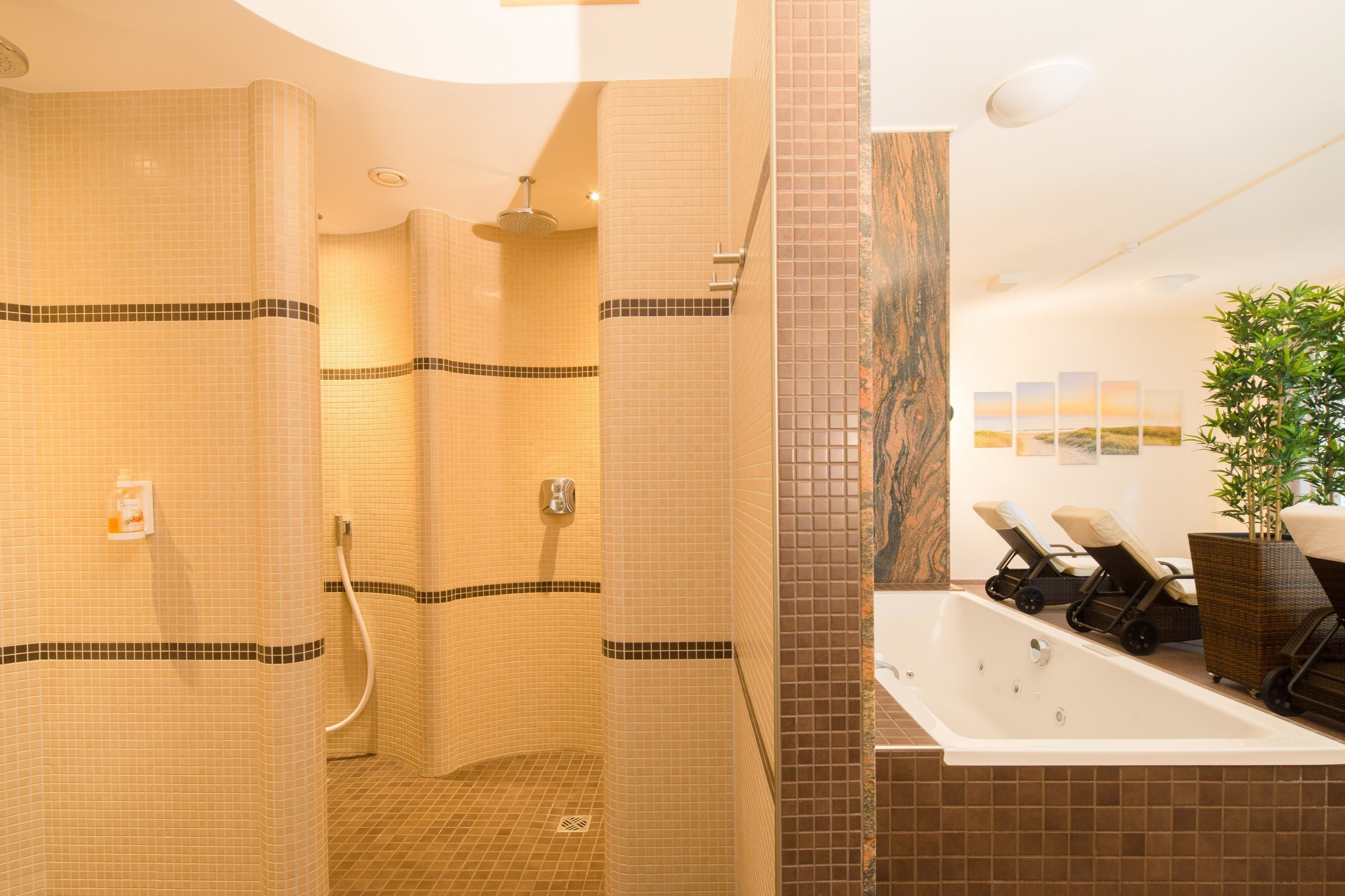 Une salle de bain moderne avec des murs carrelés, un espace douche, une baignoire et deux fauteuils.
