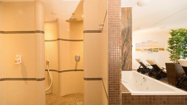 Un baño moderno con paredes de azulejos, una zona de ducha, una bañera y dos sillones de descanso.