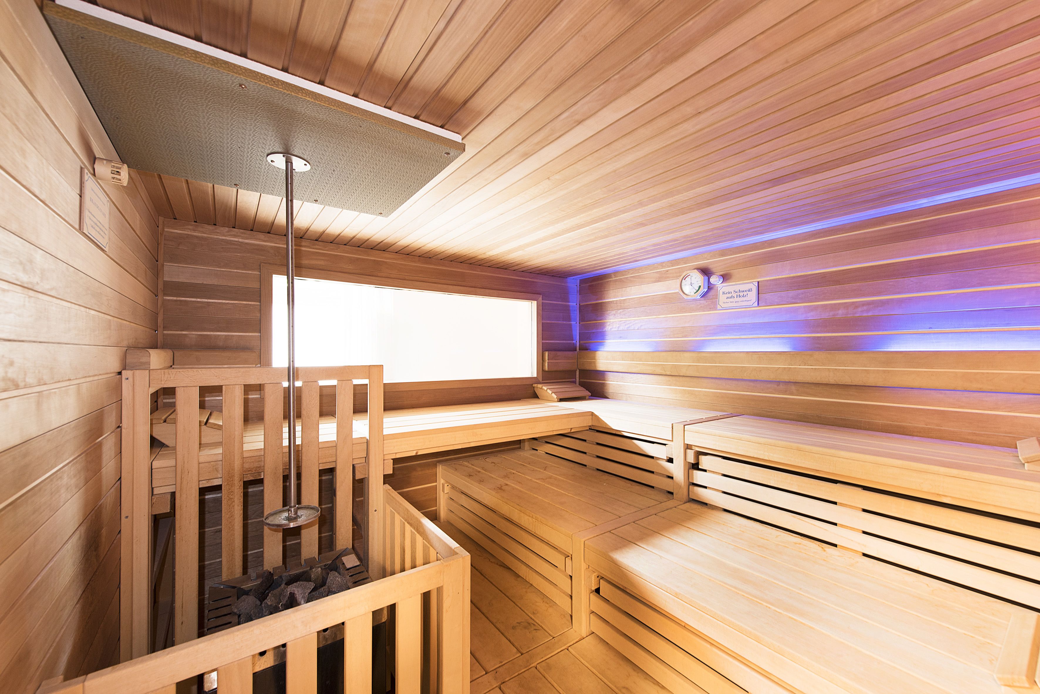 A sauna with wooden walls and benches, a ceiling light, and a clock on the wall.