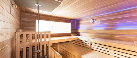 Una sauna con paredes y bancos de madera, una luz en el techo y un reloj en la pared.
