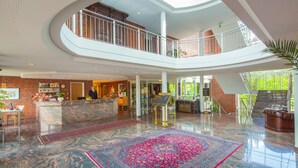 A spacious lobby with a marble floor, a reception desk, a staircase, and a high ceiling with skylights. - Hotel Heidehof Garni (Buedelsdorf)
