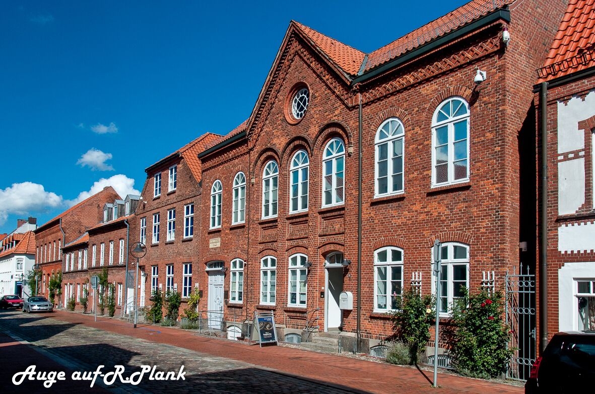 A row of red brick buildings with arched windows and a clock tower.