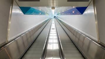 Una escalera mecánica en un espacio interior moderno y bien iluminado, con señalización digital arriba.