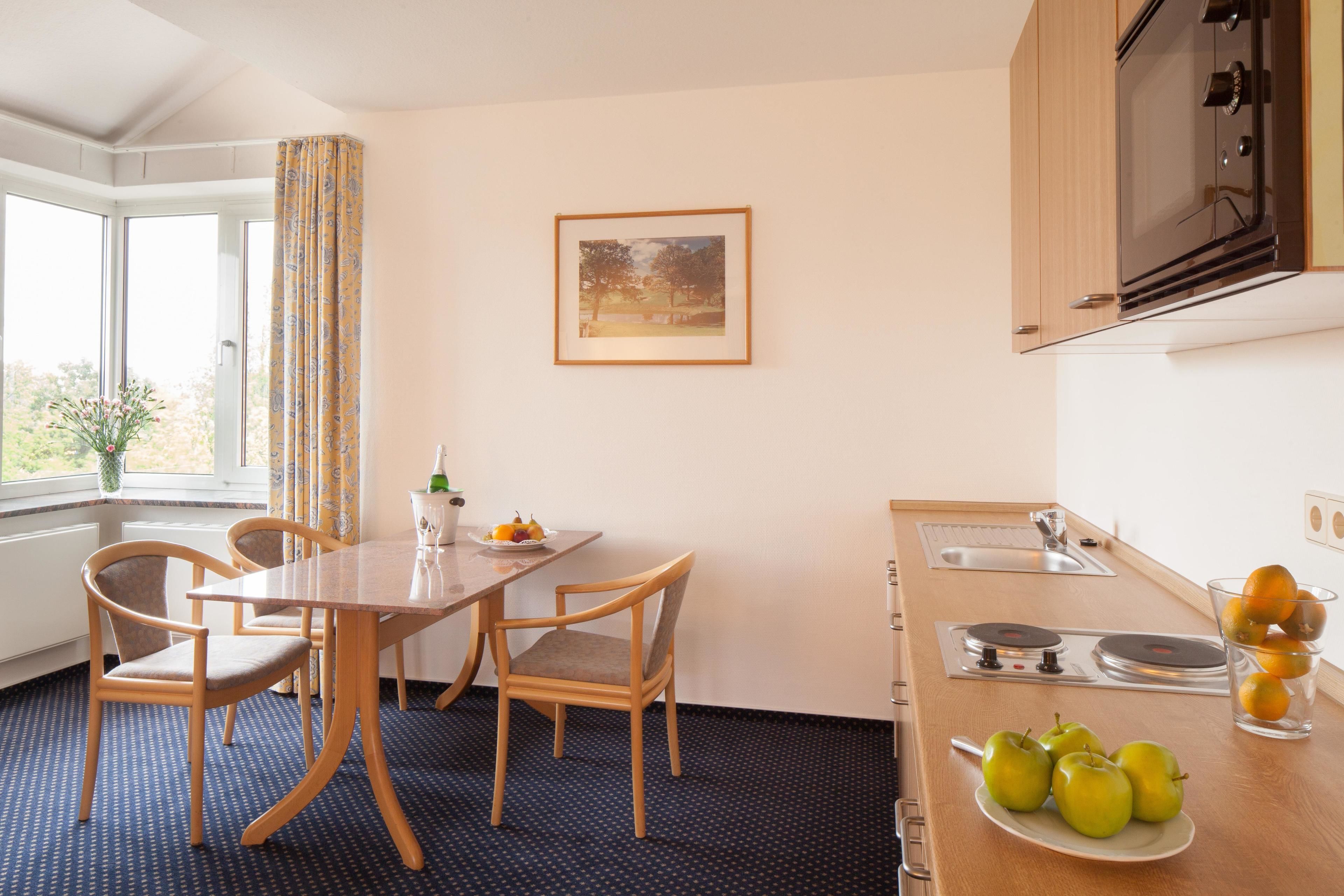 Habitación de hotel con una mesa de comedor, sillas, una zona de cocina con estufa y un ventanal con cortinas.
