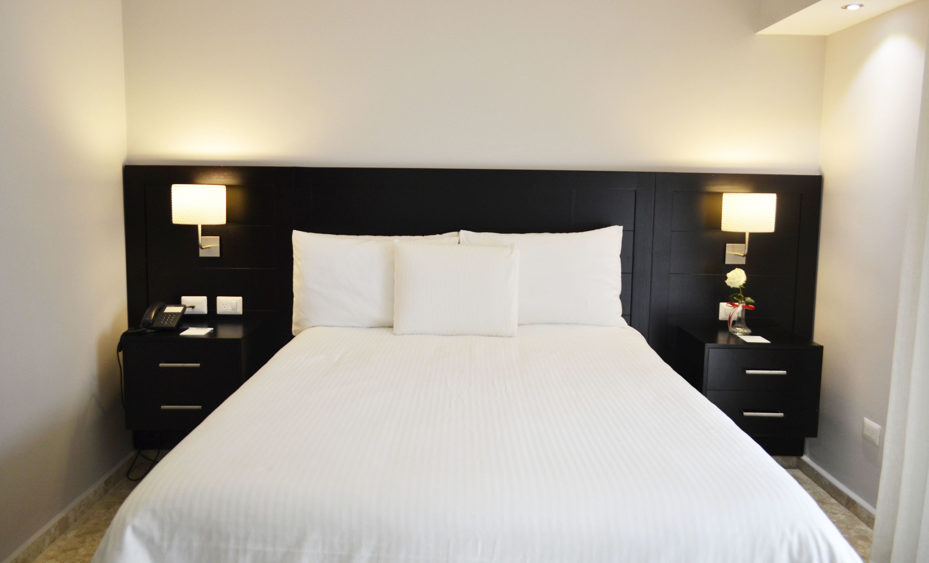 A hotel room with a large bed, two bedside tables, and two wall-mounted lamps.